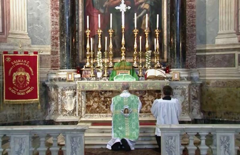 A priest kneels in front of a painting in a church.