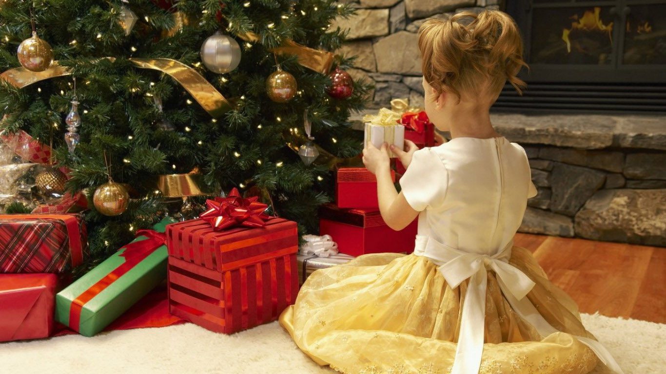 A little girl sitting on the floor next to a christmas tree.
